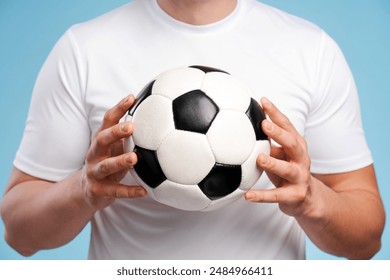 Determined athlete in a white t-shirt holds a soccer ball, showing passion for the game. Intense focus, classic colors, and blue background highlight sports excitement - Powered by Shutterstock