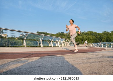 Determined Athletic Woman In Sportswear Runs On A Treadmill Over A City Bridge. Sportswoman, Female Athlete Runner Doing Morning Jog At Sunrise. Sport, Cardio Workout, Healthy Active Lifestyle Concept