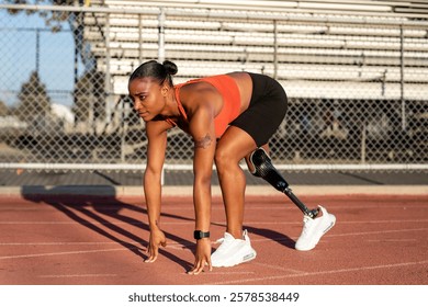 Mujer negra decidida con pierna protésica se prepara para correr en pista. Atleta amputado, fuerza y resiliencia, espíritu de determinación en el deporte. Atleta afroamericana amputada