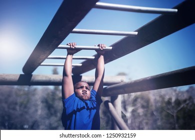Determined boy exercising on monkey bar during obstacle course in boot camp