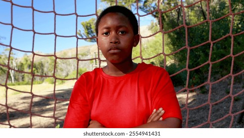 Determined boy standing with arms crossed against net during obstacle course in boot camp - Powered by Shutterstock