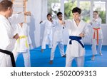 Determined boy in white kimono practicing punches in gym during martial arts workout with multiracial group of tweens. Shadow fight, combat sports training concept