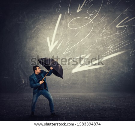 Determined businessman hiding behind umbrella as a shield to protect of any danger and high pressure of arrow sketches pointed to him. Business concept of facing adversity and auto defending.