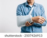 A determined businessman smiles through discomfort of broken arm, relying on treatment splint. An excited Asian man with sling support isolated on white background, emphasizing injury recovery.