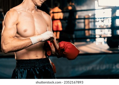 Determined Caucasian male boxer with muscularity physical readiness body wraps his hand and dons or wearing boxing glove, preparing for intense boxing training in the ring at gym. Impetus - Powered by Shutterstock