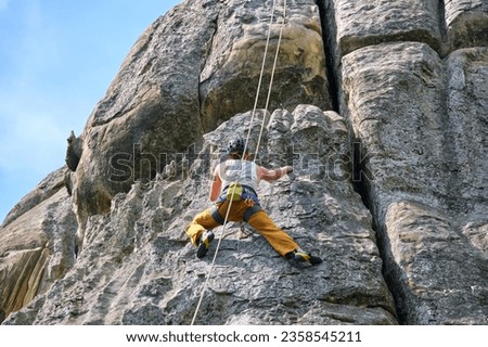 Determined climber clambering up steep wall of rocky mountain. Sportsman overcoming difficult route. Engaging in extreme sports and rock climbing hobby concept.