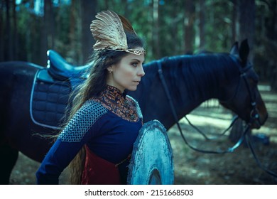 A determined and courageous beautiful woman warrior valkyrie stands with a shield next to her warhorse in a forest and looks resolutely forward. Scandinavian mythology. Epic fantasy.