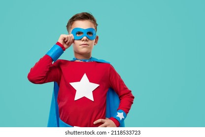 Determined courageous child in superhero cape and mask standing with hand on waist on blue background and looking away - Powered by Shutterstock