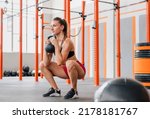 Determined female athlete looking away and doing goblet squat with heavy kettlebell during intense training in spacious light gym
