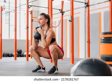 Determined Female Athlete Looking Away And Doing Goblet Squat With Heavy Kettlebell During Intense Training In Spacious Light Gym