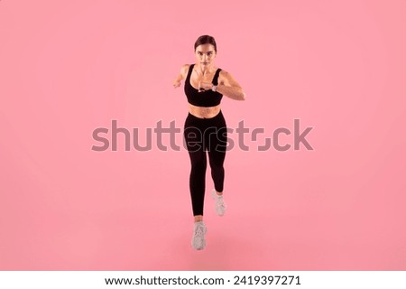 Determined female athlete running towards camera, young athletic woman doing high-energy workout session, training against soft pink studio background, full length shot with copy space