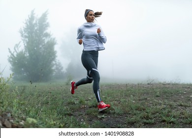 Determined female runner jogging through misty filed in the morning. Copy space. - Powered by Shutterstock