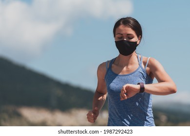 Determined fitness woman in short clothes wearing red protective face mask running outdoors in the city during coronavirus outbreak. Covid 19 and physical jogging activity, sport and fitness.