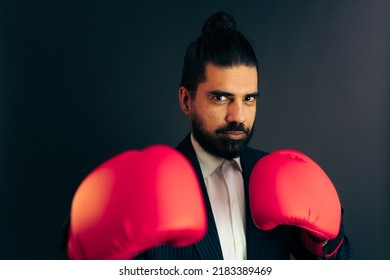 Determined Indian male boss in boxing gloves looking at camera before fight against black background - Powered by Shutterstock