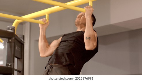 A determined individual performing pull-ups, showcasing strength and sport in a contemporary gym setting. He raises and lowers his body on his hands while hanging on the bar. His own weight.