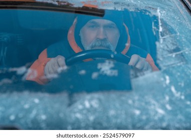 A determined man clears frost from his car window on a chilly winter morning before heading out to start the day - Powered by Shutterstock