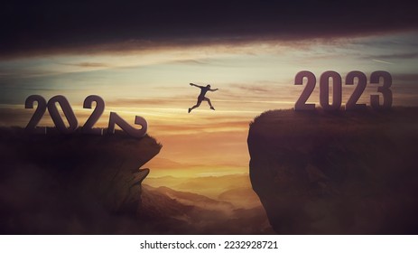 Determined man jump over a chasm obstacle to reach the new 2023 peak and let 2022 behind. Conceptual and surreal sunset scene, new year motivational background. Leader overcoming hurdles reach highs - Shutterstock ID 2232928721