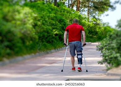 Determined Man With Knee Brace Using Crutches on a Sunny Park Pathway - Powered by Shutterstock