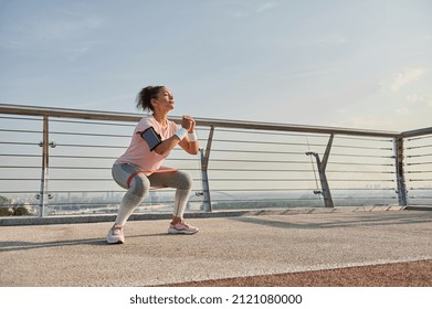 Determined middle aged sportswoman, female athlete exercising outdoor at sunrise, doing squats with elastic resistance band. Fitness sport endurance, body weight training and active lifestyle concept - Shutterstock ID 2121080000