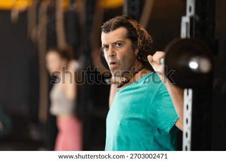 Determined middle-aged man working out with barbell in well-equipped gym during training session