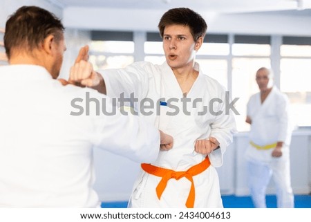 Determined motivated young karate fighter working on punches and martial arts skills in sparring with master during group training