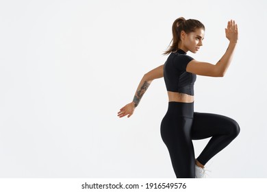 Determined muscular female athlete workout, raising leg and doing stretching exercises. Sport woman in sportswear training indoors, doing fitness aerobics, white background.