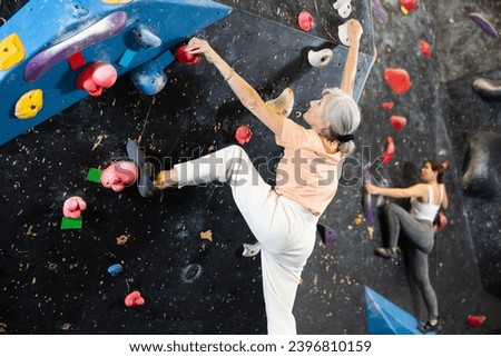 Determined old lady doing difficult wall climb in climbing gym