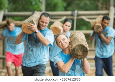 Determined people running with logs on boot camp obstacle course - Powered by Shutterstock