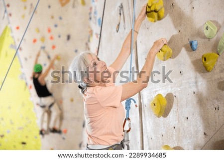 Determined senior woman doing her best at climbing artificial wall