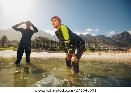 Determined sports persons standing in water getting ready for competition. Triathletes in wet suits preparing for triathlon.