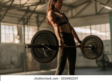 Determined and strong fitness woman training with heavy weights in fitness club. Female athlete holding heavy weight barbell in gym.
