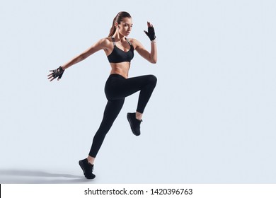 Determined to win. Full length of attractive young woman in sports clothing jumping while hovering against grey background
