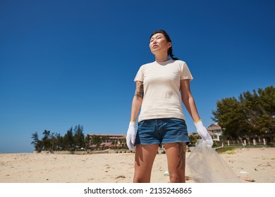 Determined Woman With Big Plastic Bag In Hand Looking At Dirty Sandy Beach With Spilled Garbage