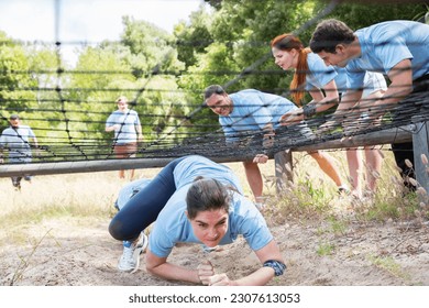 Determined woman crawling under net on boot camp obstacle course - Powered by Shutterstock