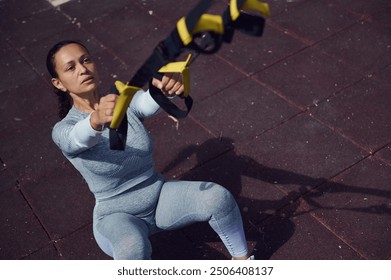 A determined woman exercises with resistance bands in an outdoor setting, emphasizing strength and fitness. She is dressed in activewear, focused on her workout routine. - Powered by Shutterstock