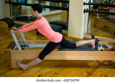 Determined woman performing stretching exercise on reformer in gym - Powered by Shutterstock