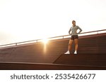 A determined woman stands proudly on a rooftop, fully embracing the warmth of the morning sun, showcasing her remarkable strength and unwavering confidence in both herself and her abilities