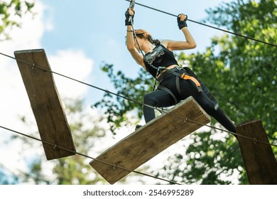 A determined woman successfully conquers the challenging high rope obstacle course set in the beauty of nature - Powered by Shutterstock