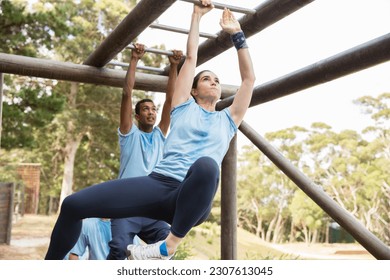 Determined woman swinging on monkey bars on boot camp obstacle course - Powered by Shutterstock