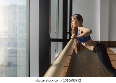 Determined working out woman pushing-up on ballet barre focused looking outside window exercising gym, warm-up before fitness, aerobics. pilates instuctor preparing muscles for training session