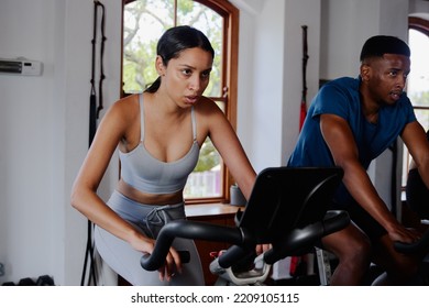 Determined Young Biracial Woman And Black Man Using Exercise Bike At The Gym