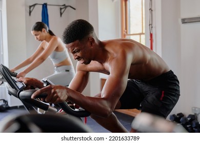 Determined Young Black Man And Biracial Woman Using Exercise Bike At The Gym