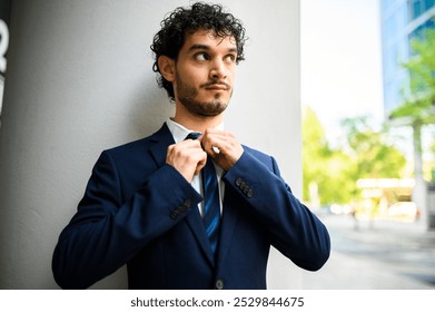 Determined young businessman adjusting his tie in the city, exuding confidence and style for a successful day at work. Urban backdrop highlights ambition and leadership - Powered by Shutterstock