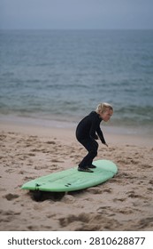 Determined young child learning how to surf, practicing balance on a surfboard 