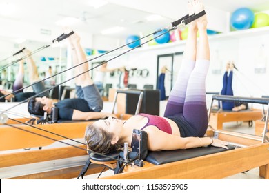 Determined young female pulling resistance bands with legs on pilates reformer in gym