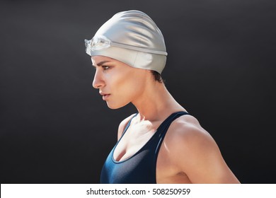 Determined Young Female Swimmer Standing Against Black Background. Fit Young Woman In Swimwear.