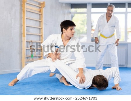 Determined young guy practicing armlock, painful control move to hold and immobilize opponent, in training bout during martial arts course in gym..