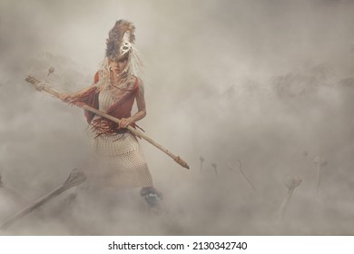 Determined young woman dressed in a wool native-style costume, standing in the fog in the middle of bones planted in the ground, firmly holding her stick, ready to defend her territory