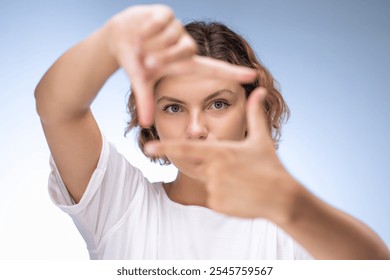 A determined young woman with short curly hair, using her hands to frame her face against a light background. Perfect for concepts of creativity, determination, and focus. High-quality stock photo - Powered by Shutterstock