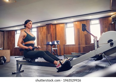 Determined Young Woman Working Out On Row Machine In Fitness Studio.